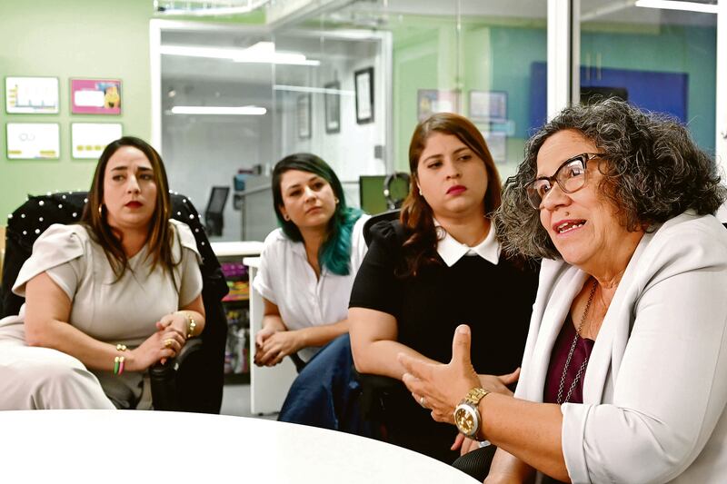 María E. Enchautegui Román conversa con el resto del equipo sentadas alrededor de una mesa blanca. El resto de las trabajadoras la miran.