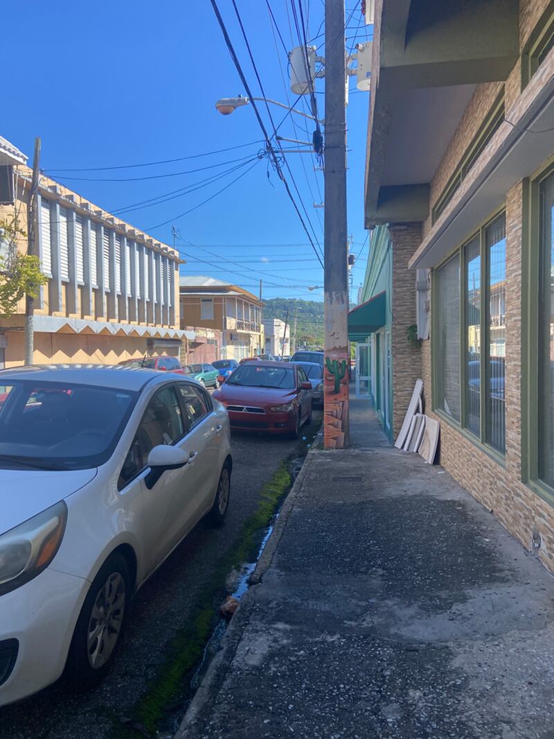 Un poste nace de una acera en el casco urbano de San Sebastián. Se observa una línea de vehículos estacionados en la orilla de la calle.