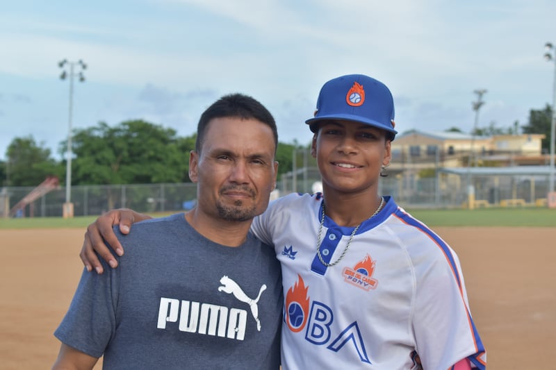 Padre e hijo sonríen a la cámara en un parque de pelota.