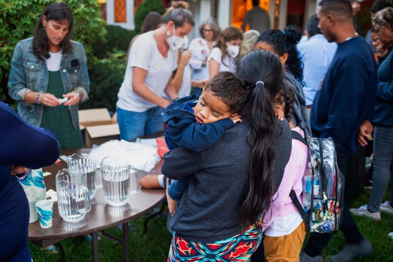 Una mujer, que está en un grupo de migrantes que fueron trasladados a Martha's Vineyard, Massachussets, carga a su hijo mientras son alimentados afuera de una iglesia.