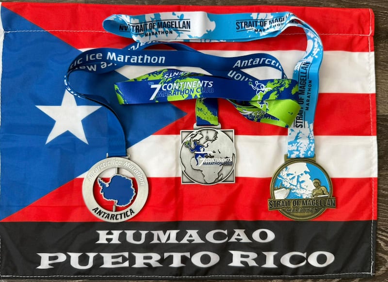 La bandera que Laboy enarboló durante el maratón y las tres medallas: la del Antarctic Ice Marathon y la de The 7 Continents Marathon Club (ambas recibidas el 13 de diciembre), junto con la tercera, correspondiente al Medio Maratón Estrecho de Magallanes en Punta Arenas, Chile (15 de diciembre).